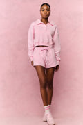 Person wearing a pink hoodie and shorts outfit against a pink background