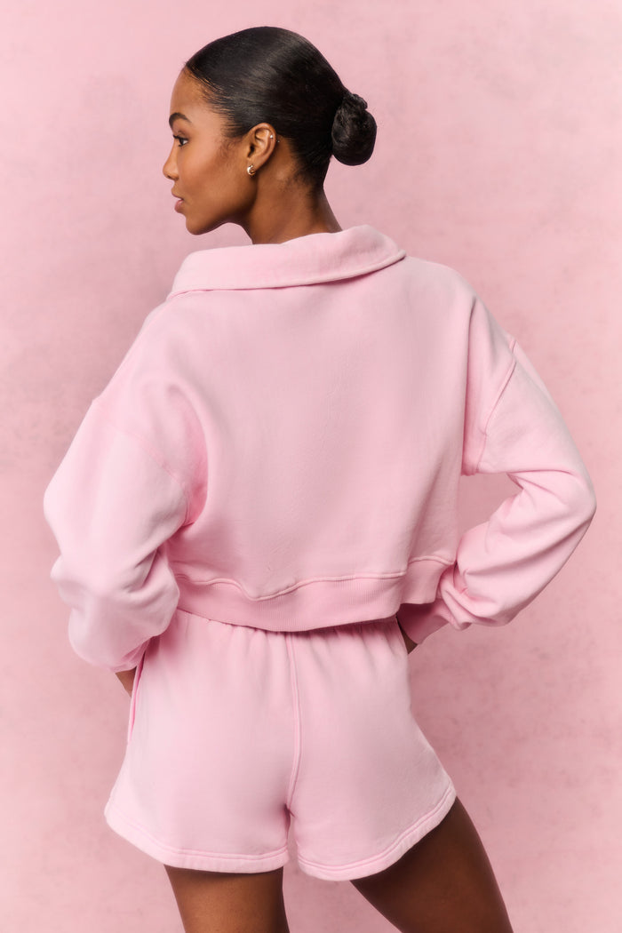 Person wearing a pink hoodie and shorts outfit against a pink background