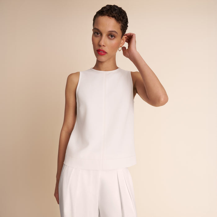 Woman wearing a white sleeveless top and pants against a beige background | Lead