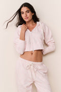 Woman wearing a light pink hoodie and pants against a plain background