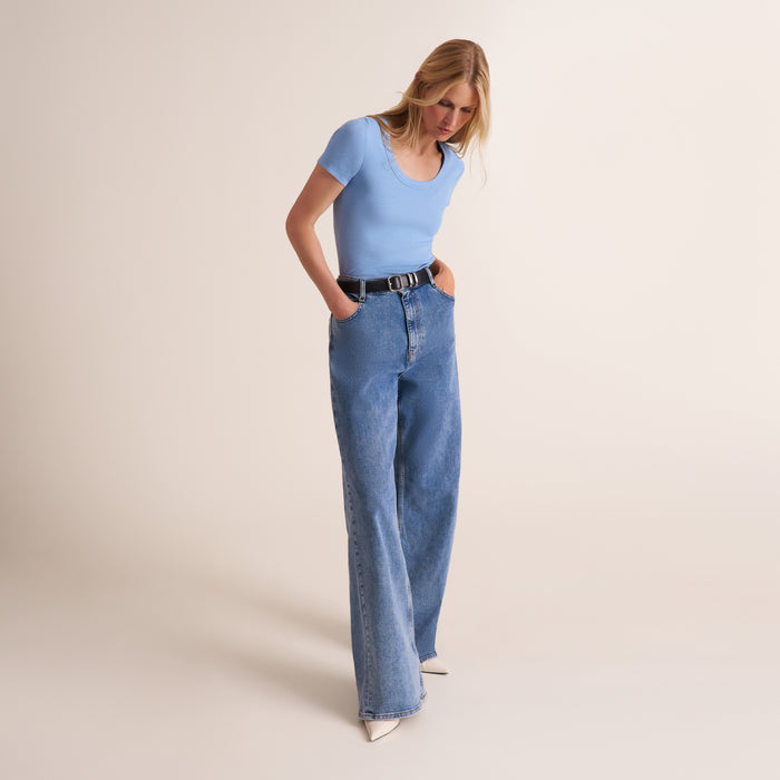 Woman wearing a light blue scoop neck short sleeve t-shirt with jeans and a belt