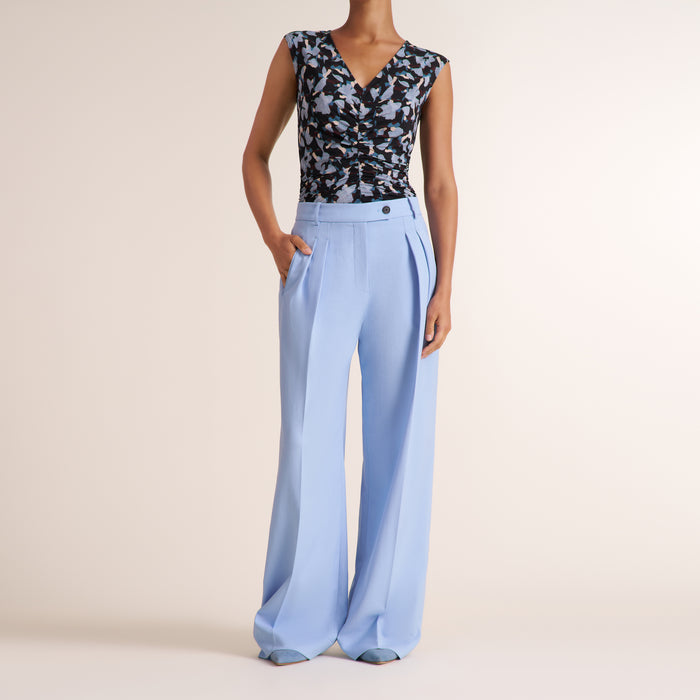 Woman wearing a light blue pant and floral top on a beige background