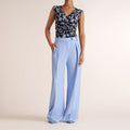 Woman wearing a light blue pant and floral top on a beige background