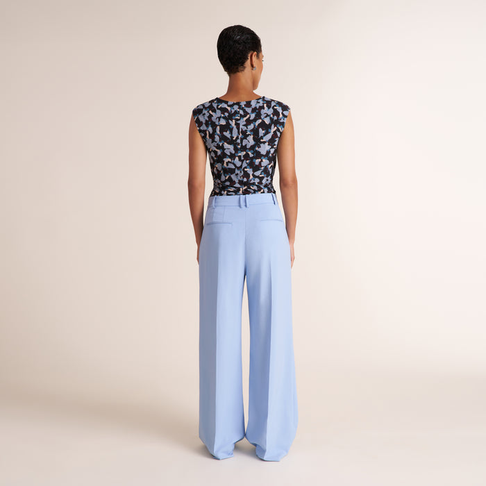 Woman wearing a light blue pant and floral top on a beige background