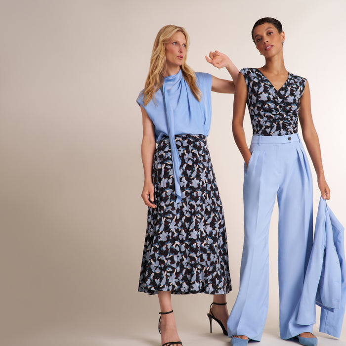 Two woman wearing light blue tops, pants, and paterned styles standing next to each other