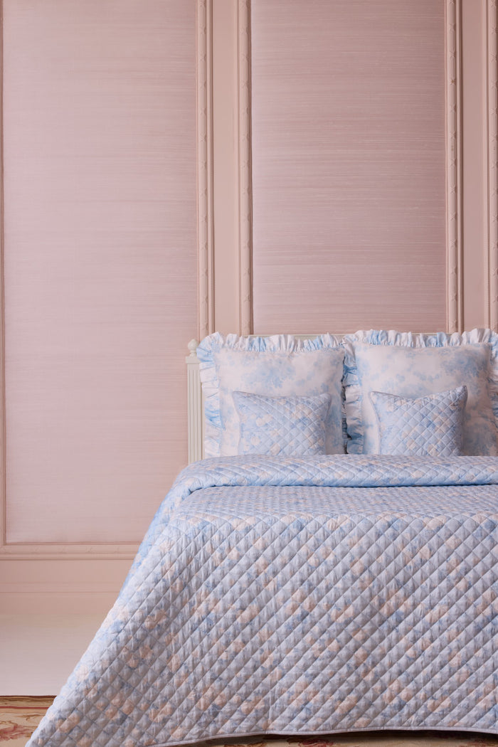 A floral printed quilt in pink and white colors displayed on a bed with matching pillowcases, against a pink paneled wall.