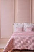 A pink floral printed quilt displayed on a bed with matching pillowcases, against a pink paneled wall.
