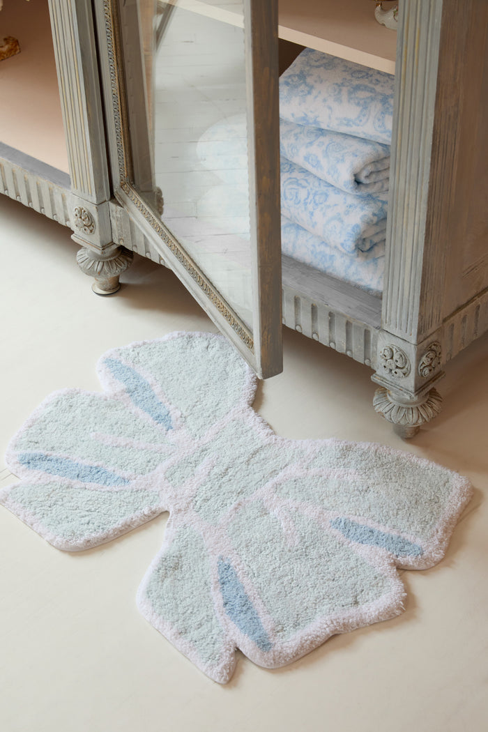 light blue bow shaped mat with a decorative pattern on a beige floor in front of a wooden cabinet.