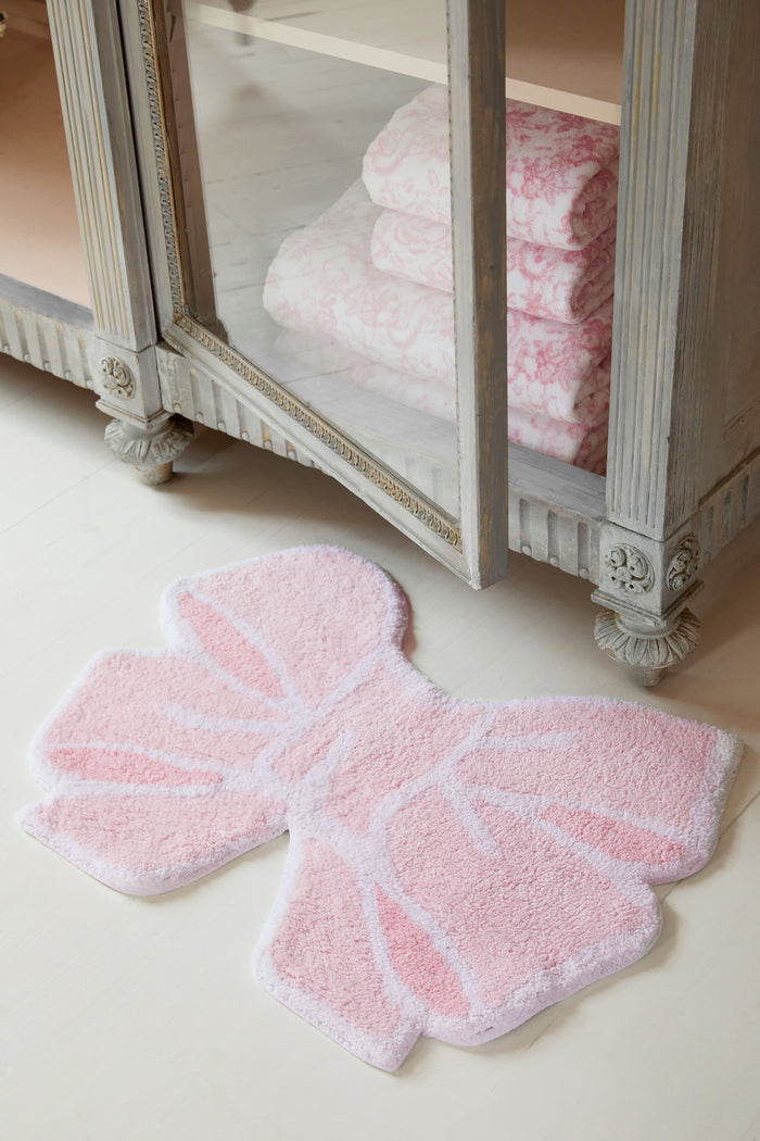 Pink bow shaped rug in front of a cabinet with pink towels.