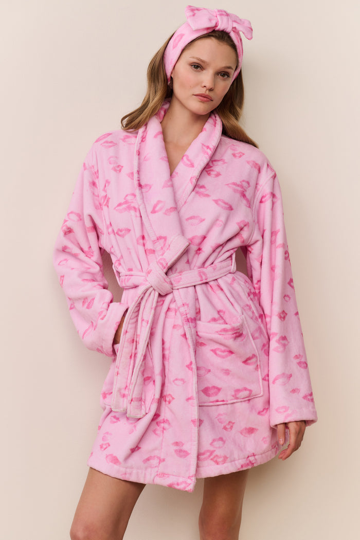 Woman wearing a pink robe with kiss print pattern and matching headband on a beige background