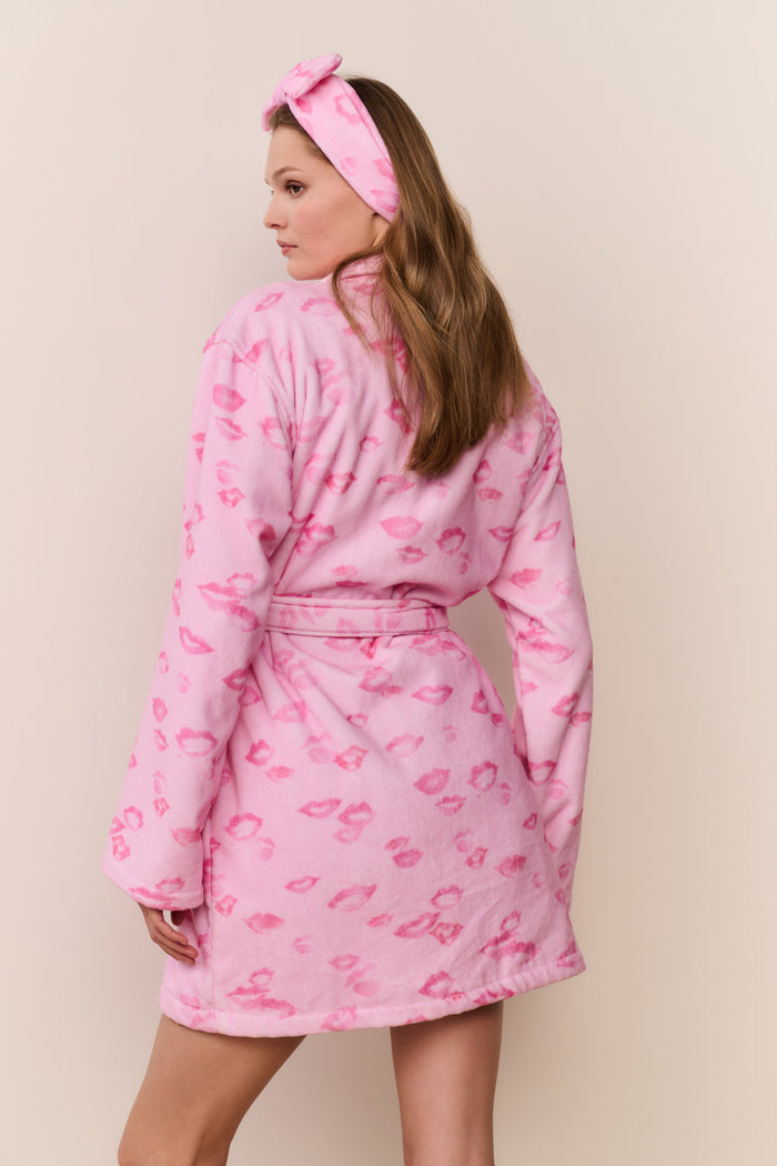Woman wearing a pink robe with kiss print pattern and matching headband on a beige background