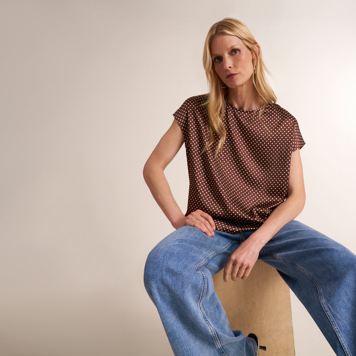 Woman wearing a pair of jeans with a cap sleeve top in a brown and white dot print | Lead