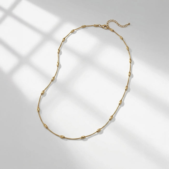 A gold chain necklace with elongated oval links, displayed on a light gray surface with soft window-box style shadows. | Lead