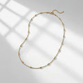 A gold chain necklace with elongated oval links, displayed on a light gray surface with soft window-box style shadows. | Lead