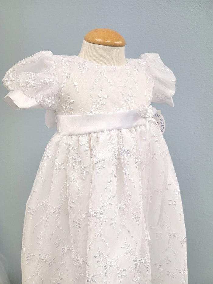 White baby gown with floral embroidery and rosette bow.