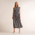 A woman modeling a sleeveless midi dress with a black and white abstract floral pattern, standing against a plain beige studio background. | Lead
