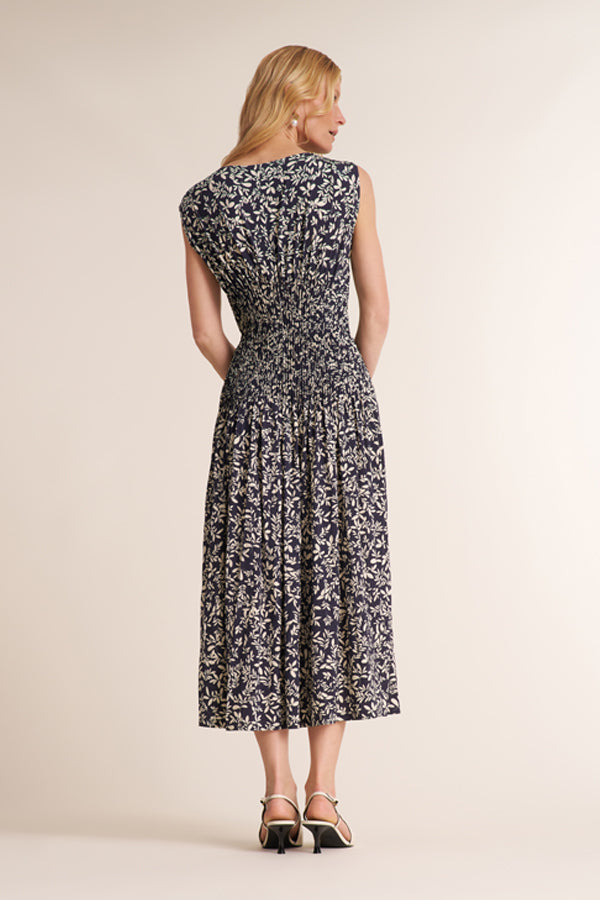 A woman modeling a sleeveless midi dress with a black and white abstract floral pattern, shown from the back against a solid beige studio background. | Exclude