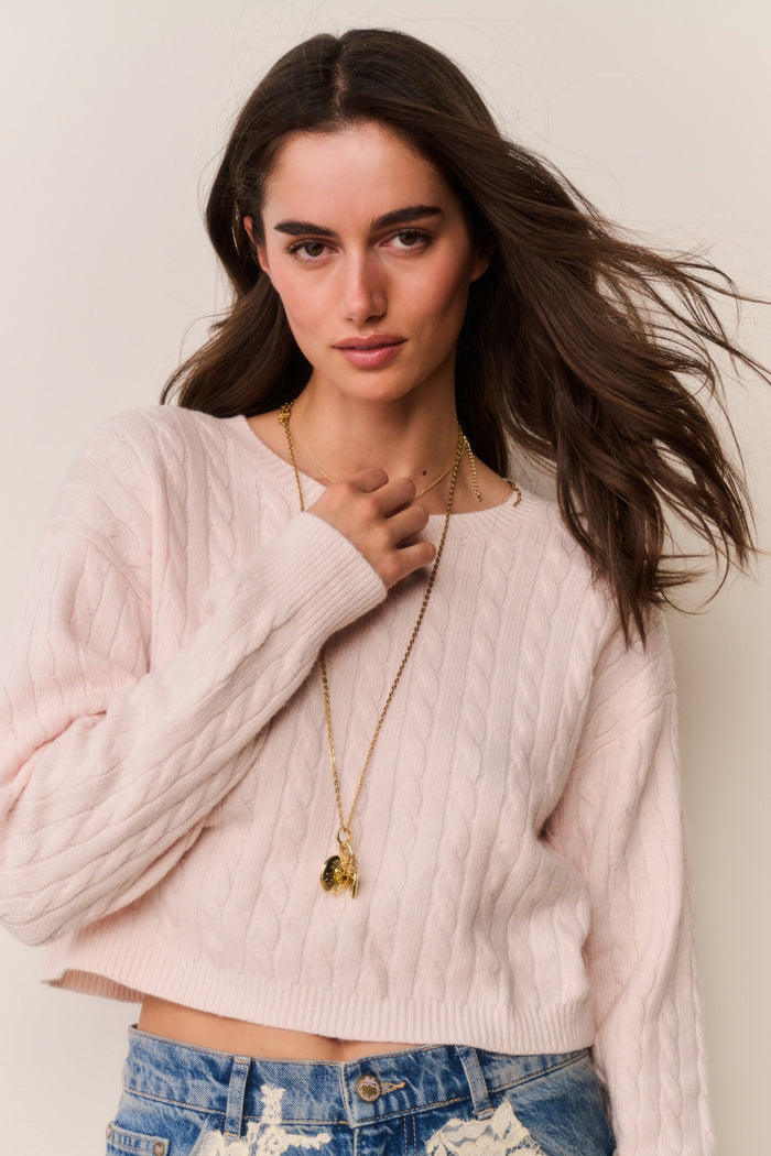 Woman wearing a light pink sweater and blue jeans with lace details against a beige background