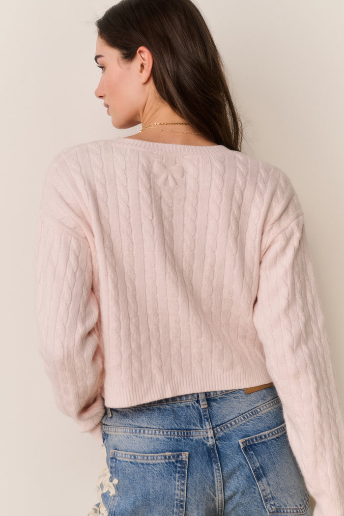 Woman wearing a light pink ribbed sweater and blue jeans against a plain background