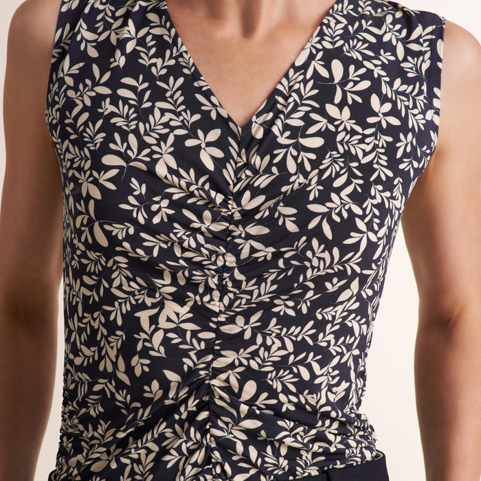 Close-up of a sleeveless V-neck top with a dark navy background and an allover cream leaf print, shown on a model.