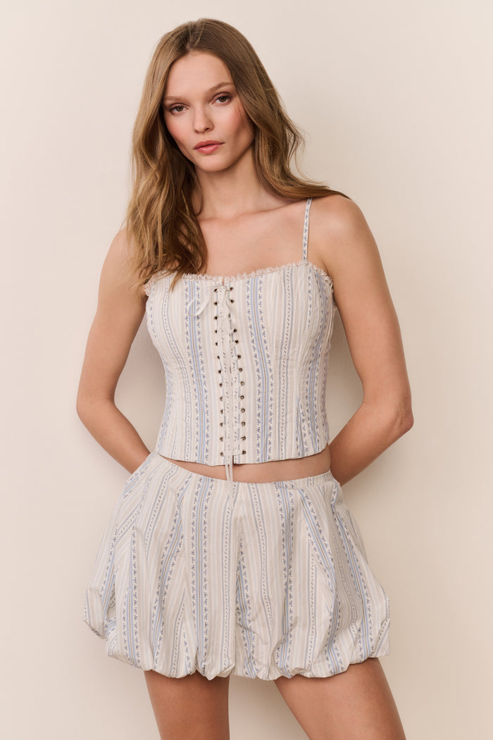 Woman wearing a striped sleeveless top with puffy striped mini skirt a on plain background