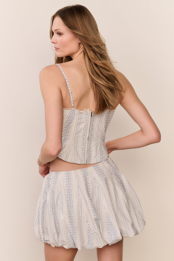 Woman wearing a striped sleeveless top with puffy striped mini skirt a on plain background