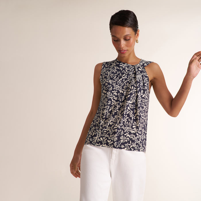 A woman modeling a sleeveless top with a navy blue and white floral pattern, paired with white pants, against a plain beige studio background. | Lead