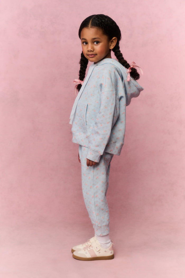 Young girl wearing a light blue tracksuit against a pink background