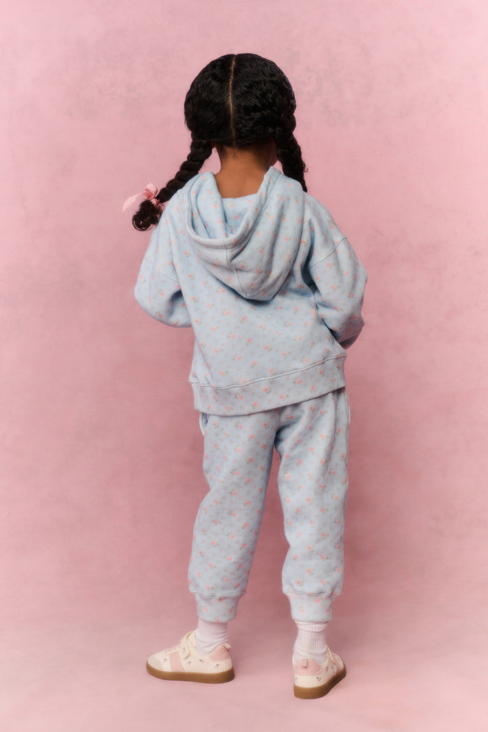 Child wearing a light blue tracksuit against a pink background