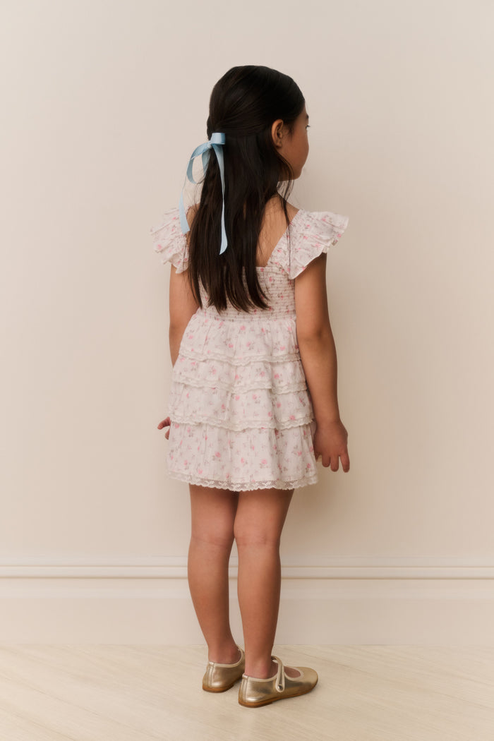 Young girl wearing a floral dress with ruffled sleeves against a plain background