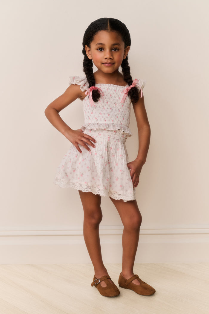 Young girl wearing a Light pink lace floral skirt and top with pink floral patterns on a plain background