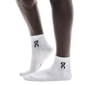 A pair of white ankle socks with the logo 'oc' printed on the side, worn on a person's foot.