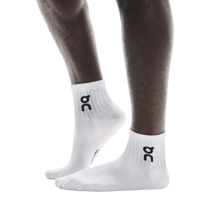 A pair of white ankle socks with the logo 'oc' printed on the side, worn on a person's foot.