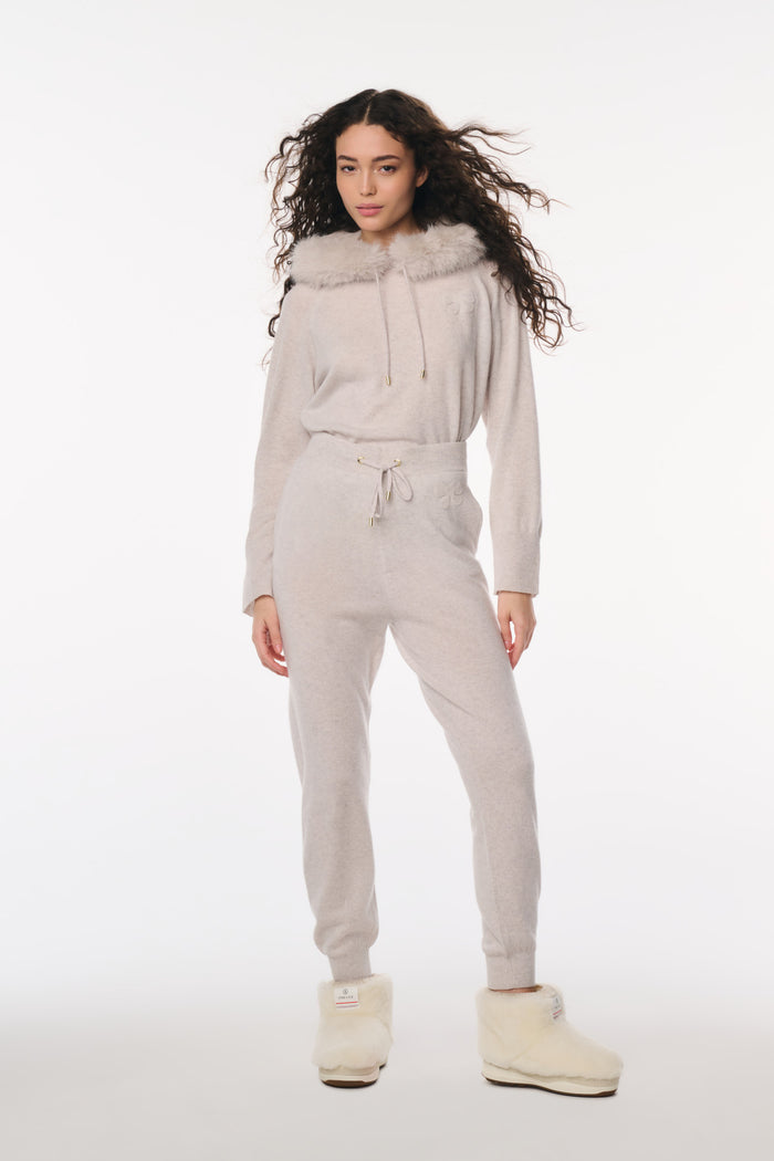Woman wearing a light gray hoodie and pants set with fur-lined hood on a white background
