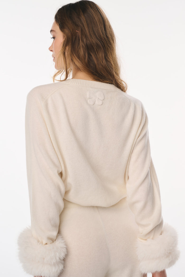 Woman wearing a cream-colored outfit with fur trim on a white background