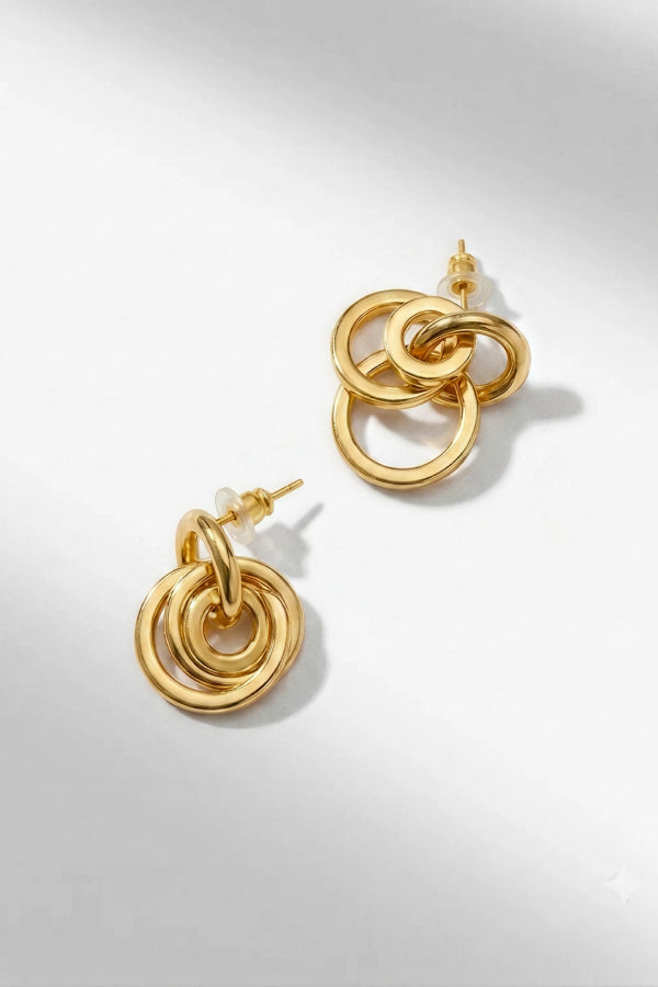A pair of gold-toned dangle earrings with interlocking circular ring designs, displayed on a clean white background with soft shadows. | Grid | Exclude