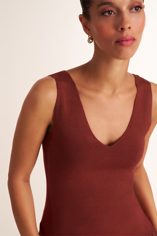 A close-up of a woman wearing a sleeveless deep V-neck bodysuit in a rich burgundy or rust red color, set against a plain light beige studio background. | Exclude
