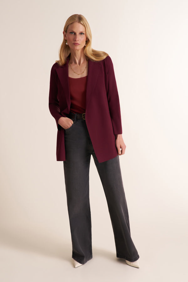 A woman modeling a burgundy open-front blazer over a matching burgundy top, paired with dark charcoal wide-leg trousers and white pointed-toe heels, against a plain beige studio background. | Exclude
