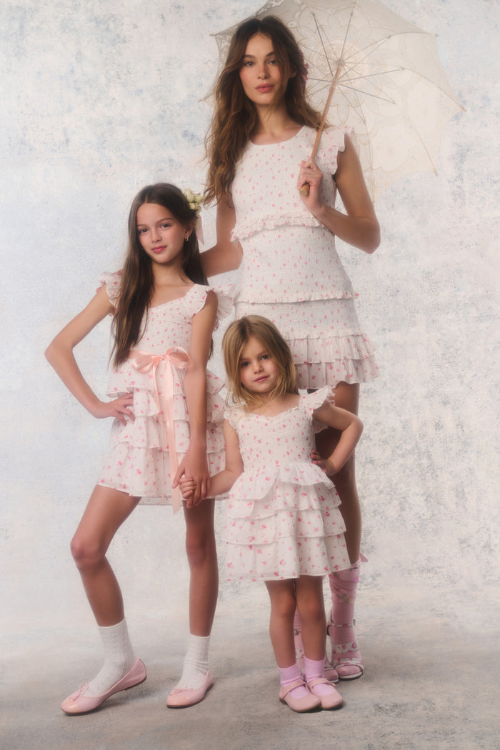 Three women in white lace dresses standing together against a textured white background.