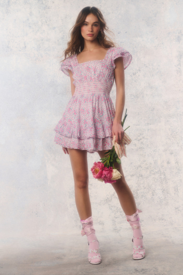 Woman in a pink floral dress holding flowers against a light background