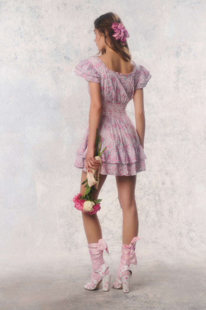 Woman in a pink dress with puffed sleeves and matching shoes holding flowers against a light background