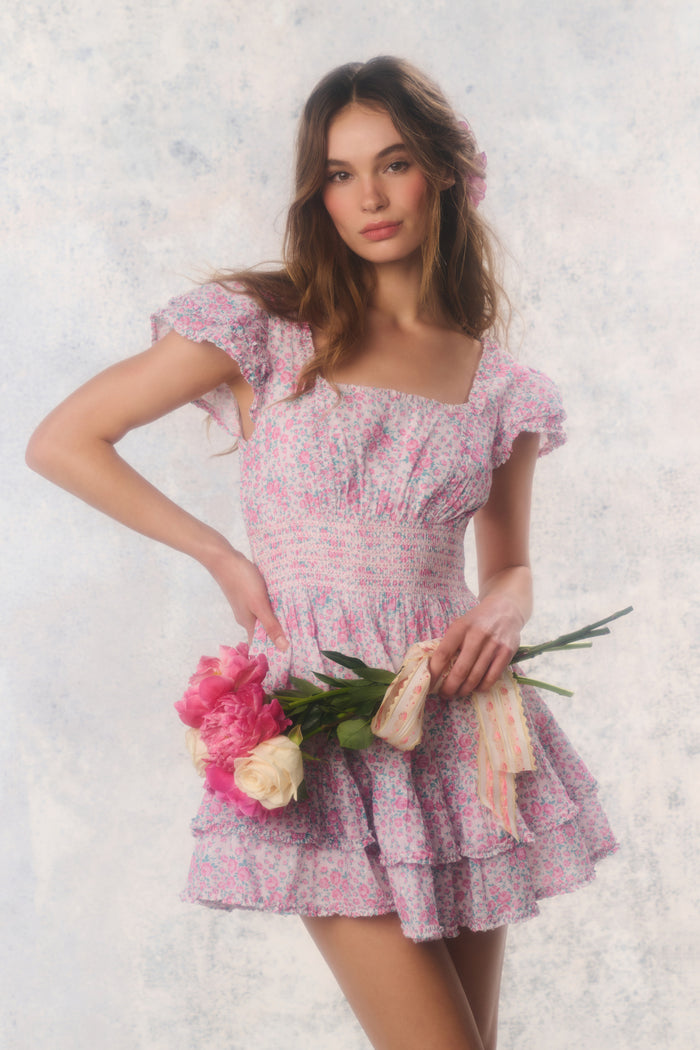 Woman in a floral dress holding flowers against a textured white background