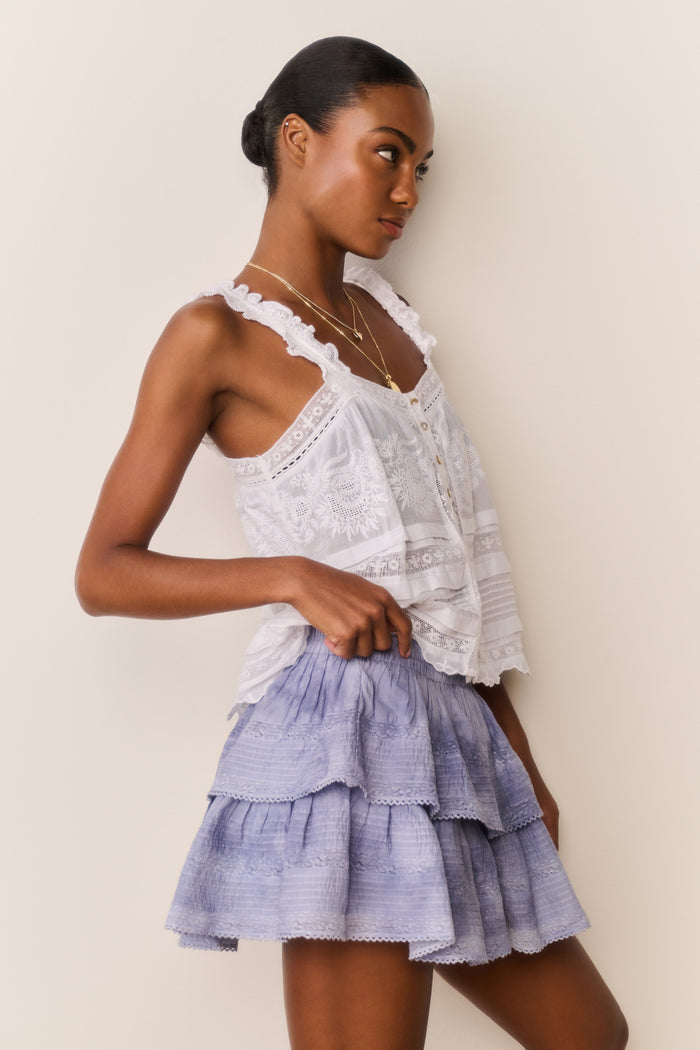Woman wearing a white lace top and blue ruffled tie-dye skirt against a beige background