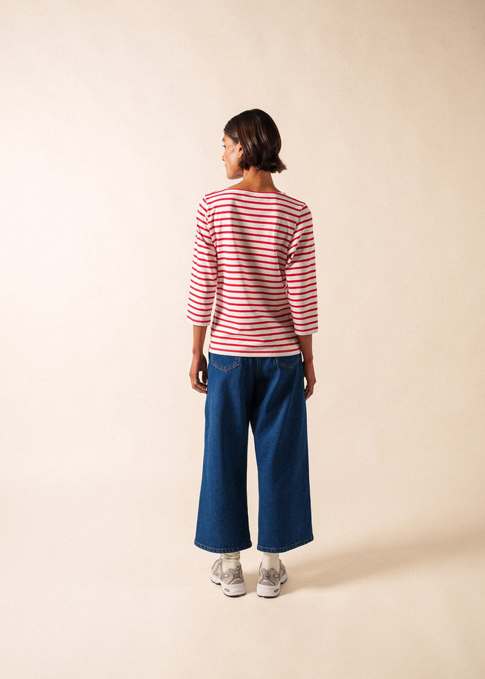 Person wearing a red and white striped shirt and blue jeans on a beige background