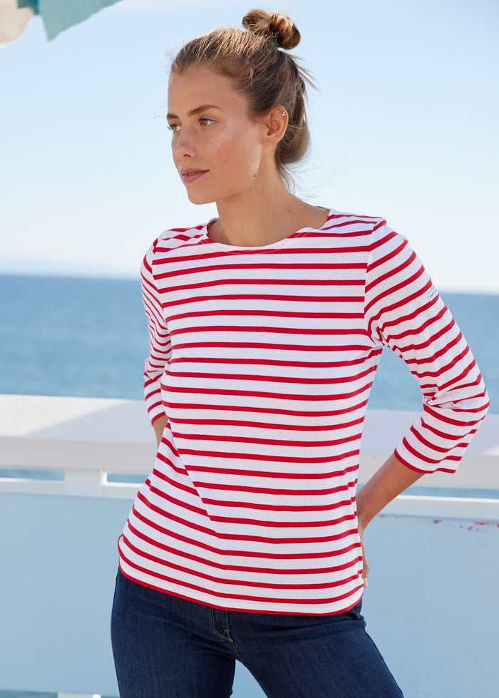 Woman wearing a red and white striped shirt with blue jeans by the sea.