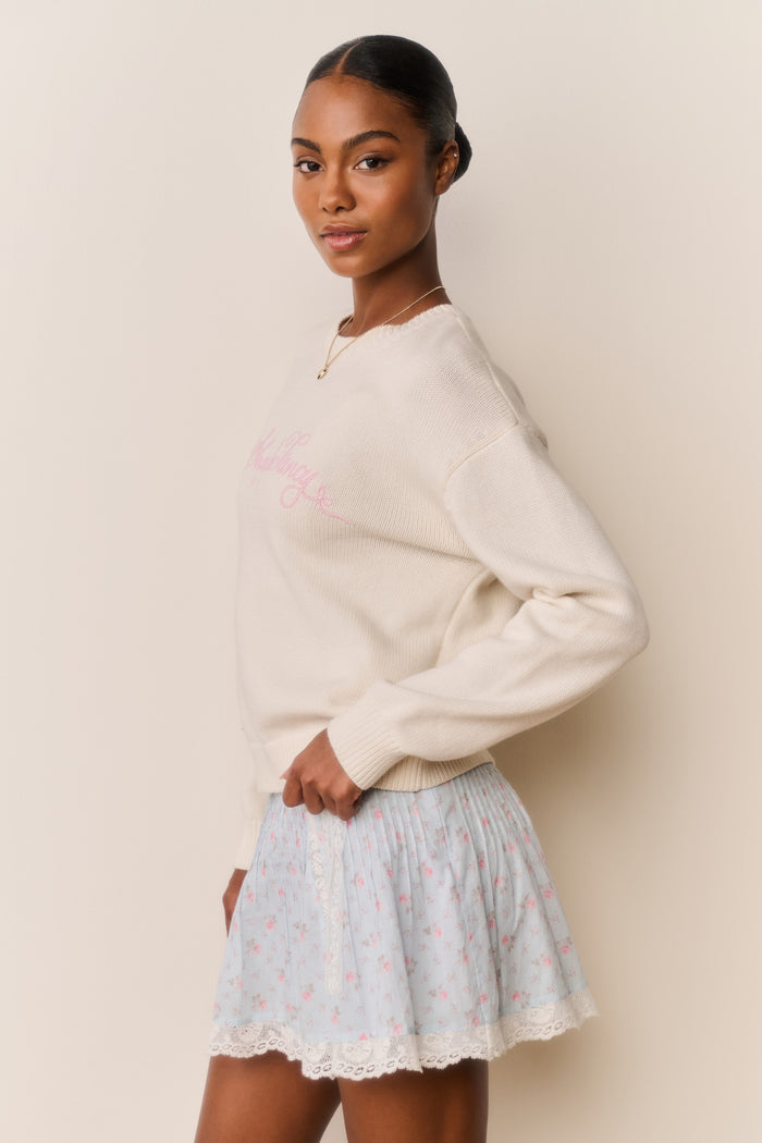 Woman wearing a beige sweater and light blue floral skirt against a plain background