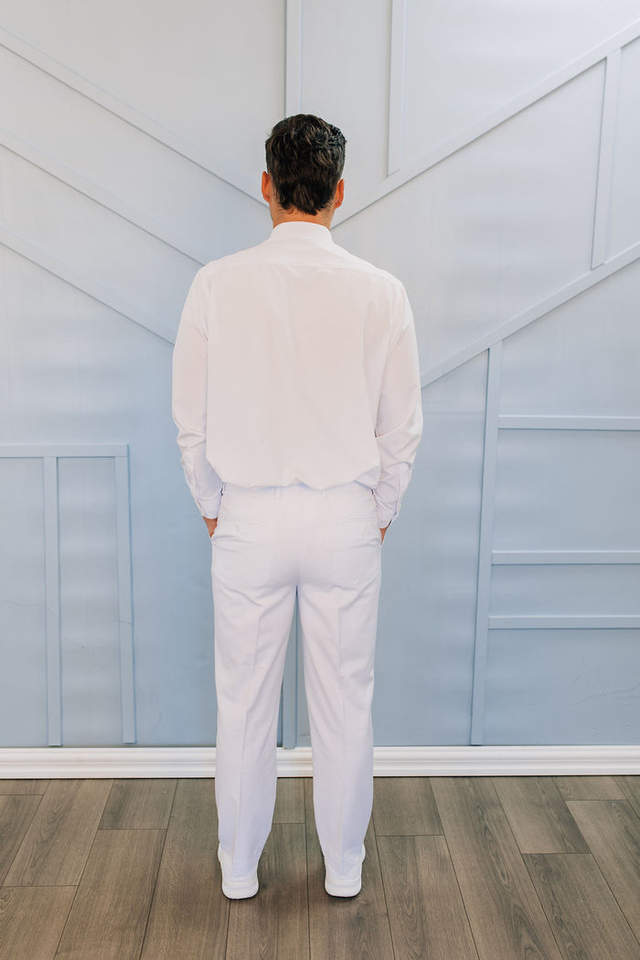 Man in all white pants, button up shirt, tie, and suspenders.