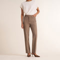 A model from the back wearing high-waisted taupe straight-leg trousers, a white draped short-sleeve top, and brown pointed-toe slingback heels against a warm off-white studio background. | Lead