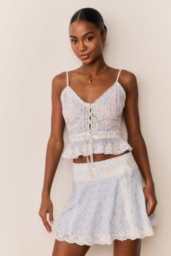 Woman wearing a Skirt and top with blue floral pattern and white lace trim with a beige background