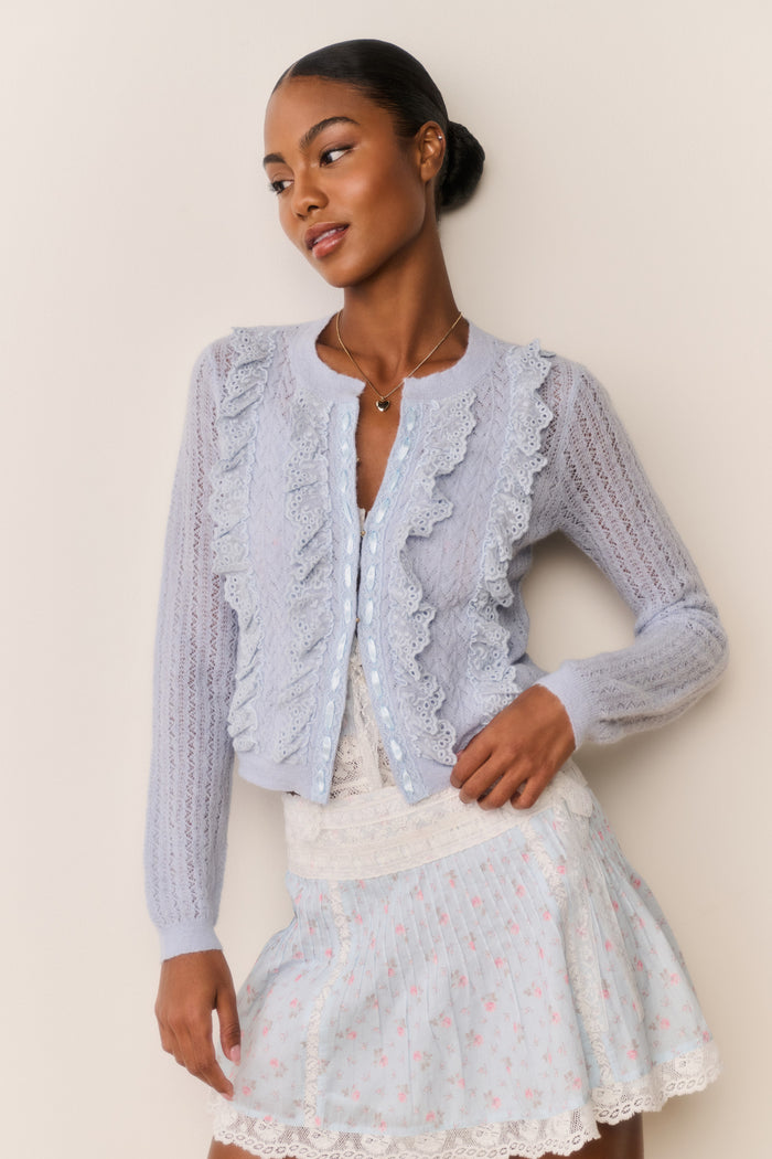 Woman wearing a Skirt and top with blue floral pattern and white lace trim with a beige background